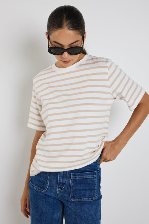 Model wears a white and ecru stripe shirt with blue jeans 