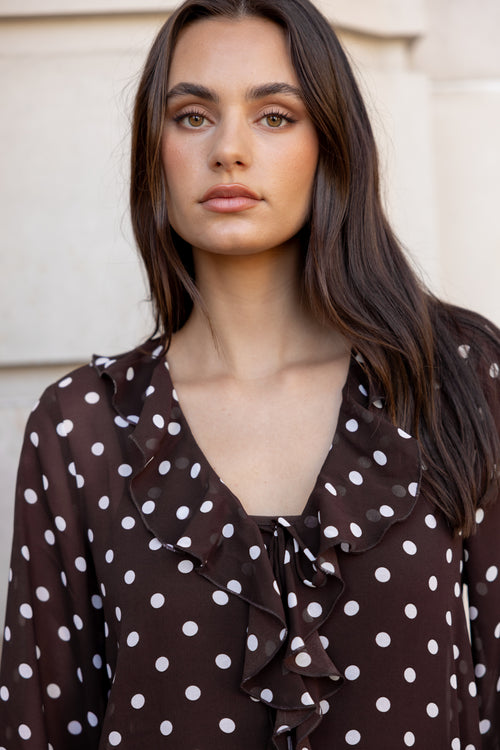 Woman wearing a brown polka dot blouse against a neutral background