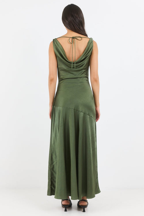 A woman viewed from the back wearing a sleeveless olive green maxi dress with a draped cowl neckline and tie detail at the back, paired with black heeled sandals against a plain white studio background.