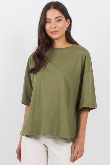 A woman modeling an oversized olive green short-sleeve top and off-white wide-leg pants against a clean white studio background.