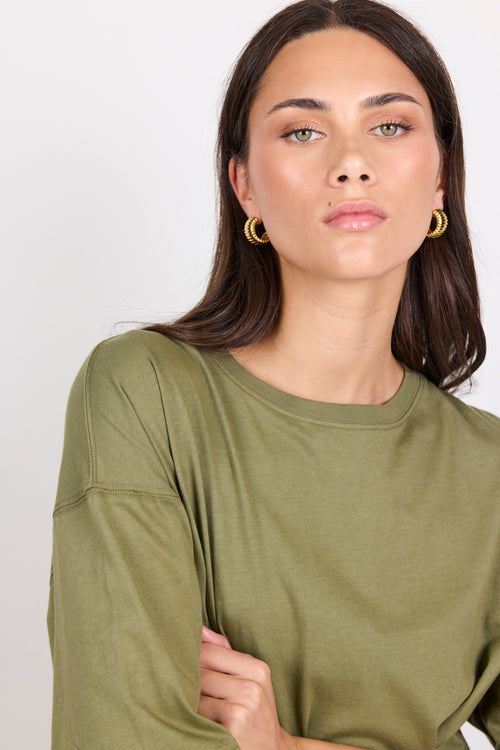 Woman wearing an olive green short-sleeve top against a white background