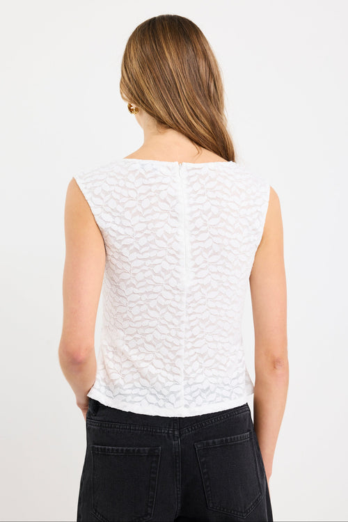 Woman wearing a sleeveless ivory lace top with subtle leaf pattern, zip-back, and fitted silhouette, paired with black jeans.
