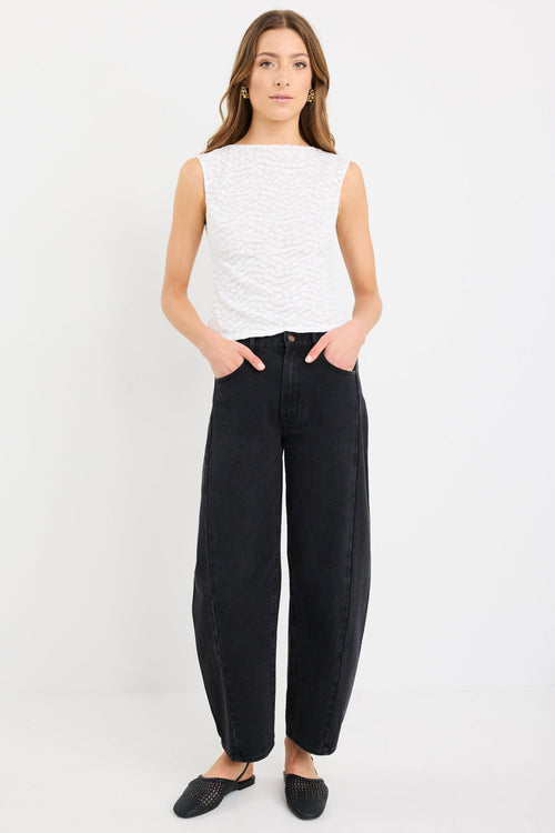 Woman wearing a sleeveless ivory lace top with subtle leaf pattern, zip-back, and fitted silhouette, paired with black jeans.