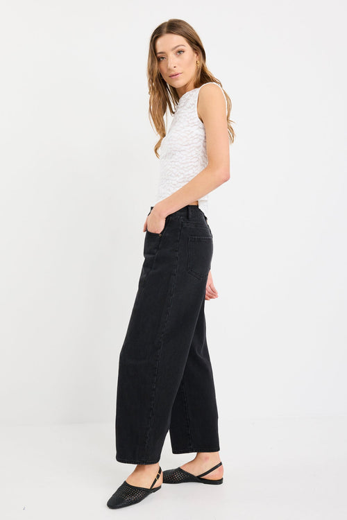 Woman wearing a sleeveless ivory lace top with subtle leaf pattern, zip-back, and fitted silhouette, paired with black jeans.