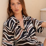 Woman sitting on a staircase wearing a zebra-striped shirt and denim shorts.