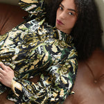 Woman in a patterned outfit sitting on a brown leather couch.
