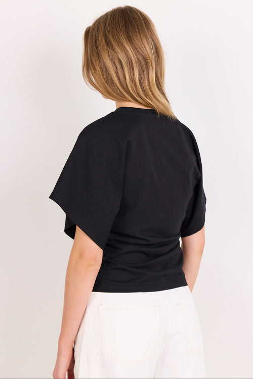 A woman viewed from the back wearing a black short-sleeve crop top and white pants against a plain light background.