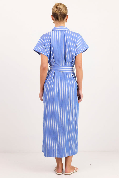 A woman viewed from behind wearing a blue and white vertically striped short-sleeve shirt dress with a matching tie belt, standing against a plain white studio background.