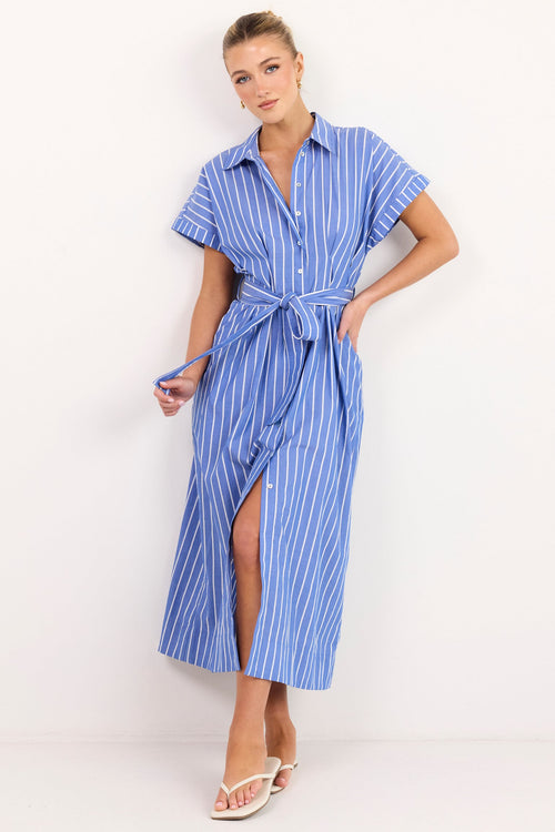 A woman modeling a blue and white vertically striped midi shirt dress with short sleeves, a button-up front, and a matching tie belt, standing against a plain white studio background.