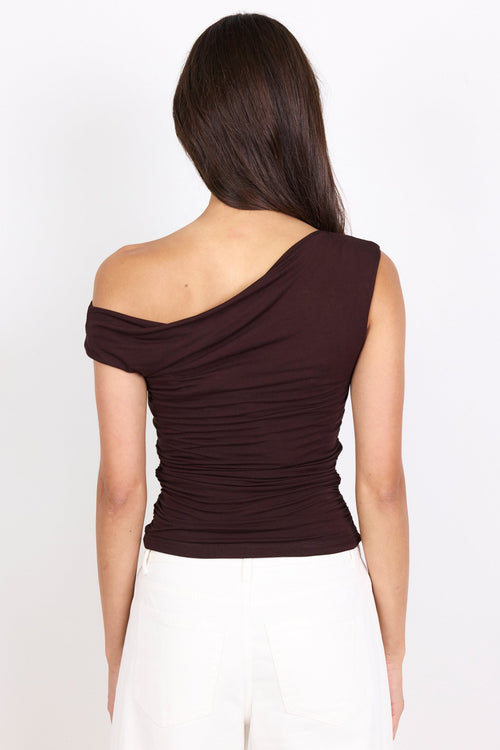 A woman shown from the back wearing a dark brown off-the-shoulder ruched top and white pants against a plain white background.