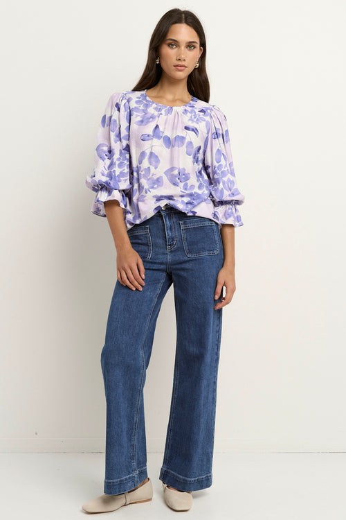 Model wears a white and blue floral blouse with dark blue jeans
