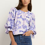 Model wears a white and blue floral blouse with dark blue jeans