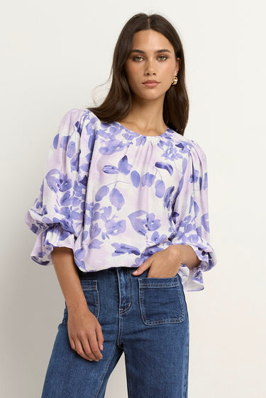 Model wears a white and blue floral blouse with dark blue jeans