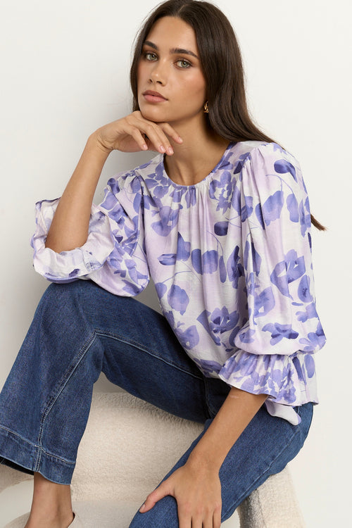 Model wears a white and blue floral blouse with dark blue jeans