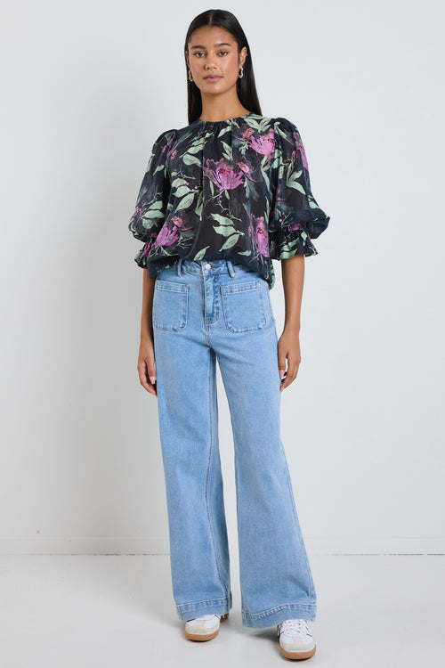 Model wears a black floral mid sleeve blouse top with blue jeans. 