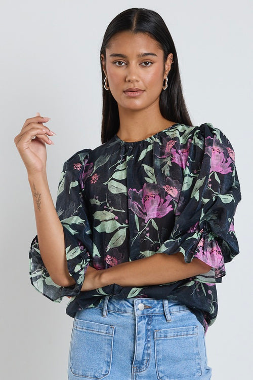 Model wears a black floral mid sleeve blouse top with blue jeans. 