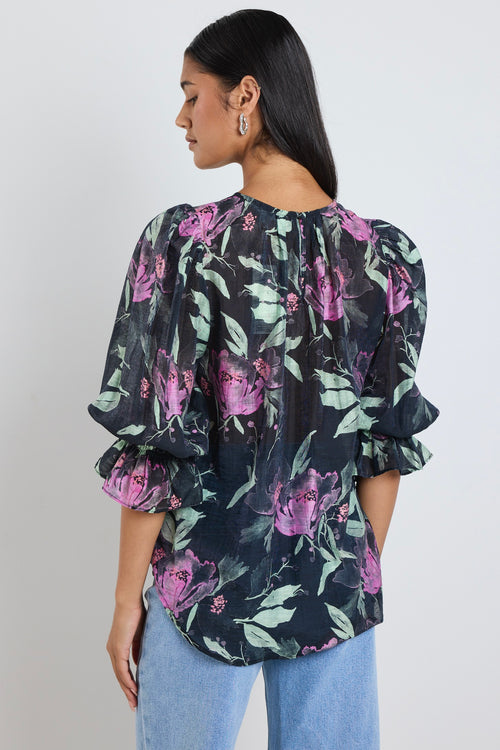 Model wears a black floral mid sleeve blouse top with blue jeans. 