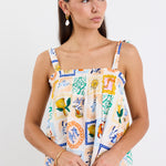 Woman wearing a colourful printed babydoll cami with tie straps, shirred neckline, and a loose, flowy fit paired with blue jeans.