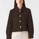 Woman wearing a brown jacket and beige pants on a white background