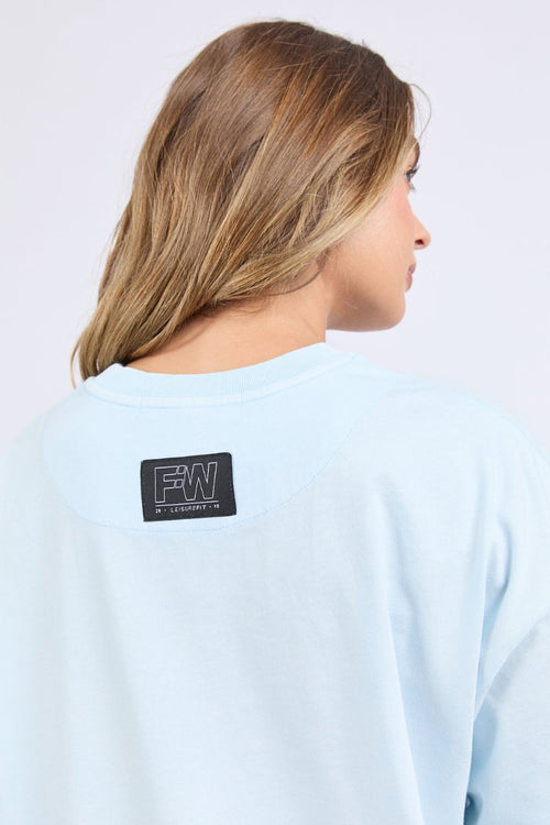 Woman wears an oversized pale blue t-shirt with short sleeves, a round neckline, and small 