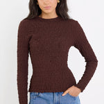 Woman wearing a brown ribbed sweater and blue jeans on a white background