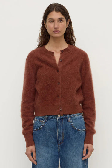 Woman wearing a brown cardigan and blue jeans against a white background