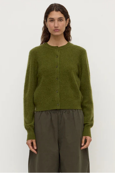 Person wearing a green cardigan and brown pants against a white background