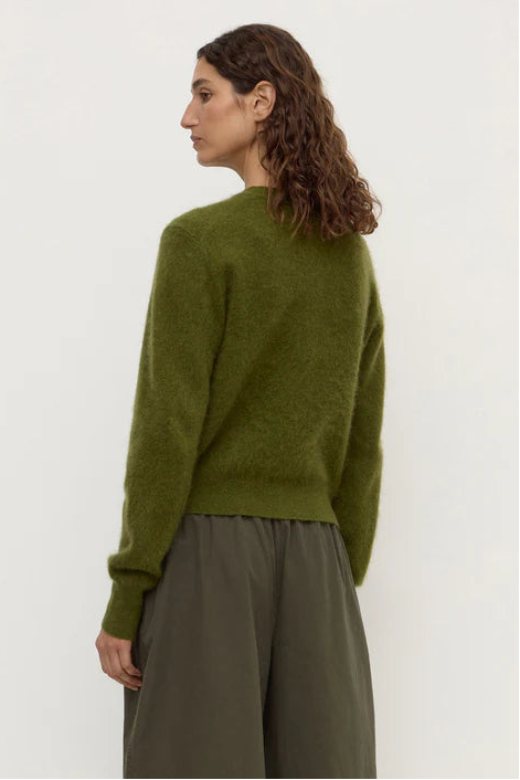 Woman wearing a green sweater and brown pants against a white background