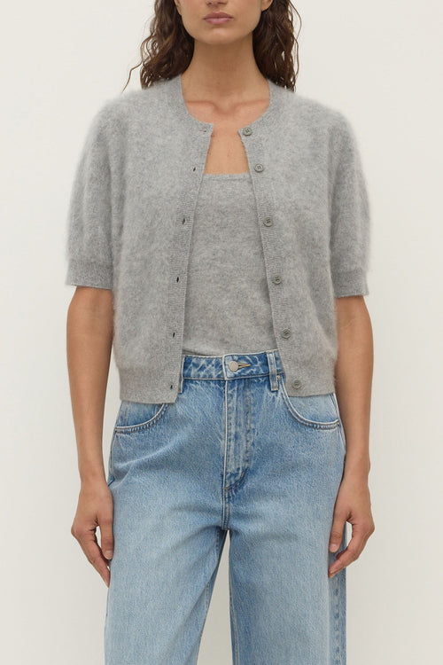 Person wearing a gray cardigan over a light blue top and jeans on a plain background