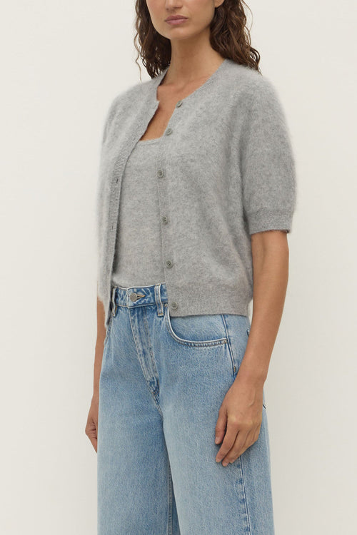 Person wearing a gray cardigan and light blue jeans on a white background