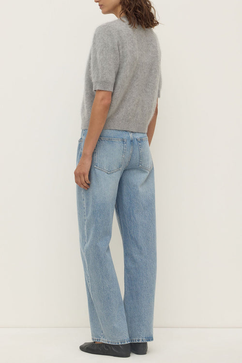 Person wearing a gray sweater and light blue jeans on a white background