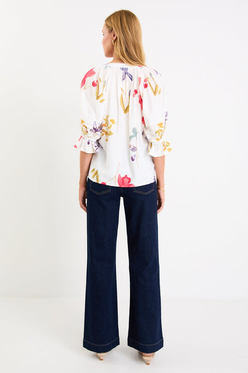 Woman wearing a cream floral poppy top and blue jeans
