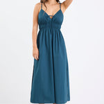 Woman wearing a petrol blue strappy cotton midi dress with a tie detail at the bust, gathered waist, and side splits.
