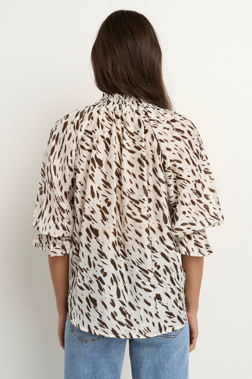 Woman wearing a loose animal-print blouse with ruffled collar and blue wide-leg jeans.