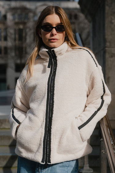 Woman wearing a white fleece jacket with black zipper and trim, standing outdoors.