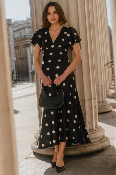 Woman in a black polka dot dress standing between classical columns.