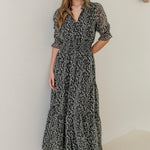 Woman wearing a charcoal animal print short sleeve dress with shirred bodice and tiered skirt, styled with black heels.