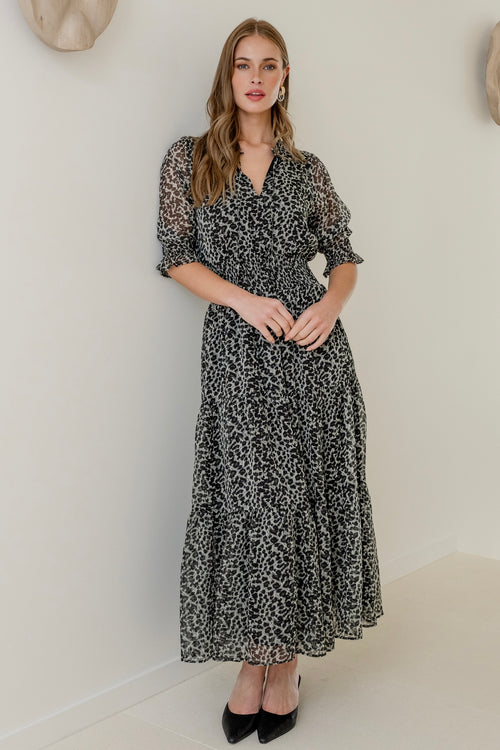 Woman wearing a charcoal animal print short sleeve dress with shirred bodice and tiered skirt, styled with black heels.