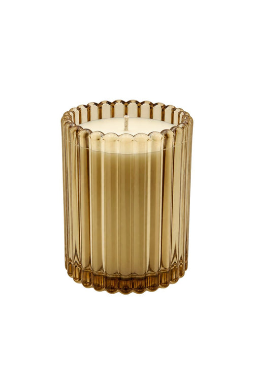 A single lit candle in a ribbed, fluted amber glass holder, shown against a plain white background.