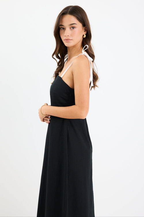 Woman wearing a black and white colour-block strappy maxi dress with tie straps, fitted bodice, and flared hem.