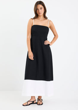 Woman wearing a black and white colour-block strappy maxi dress with tie straps, fitted bodice, and flared hem.