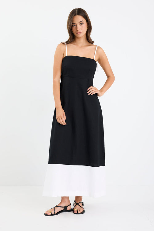 Woman wearing a black and white colour-block strappy maxi dress with tie straps, fitted bodice, and flared hem.
