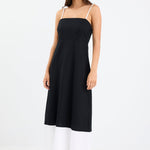 Woman wearing a black and white colour-block strappy maxi dress with tie straps, fitted bodice, and flared hem.