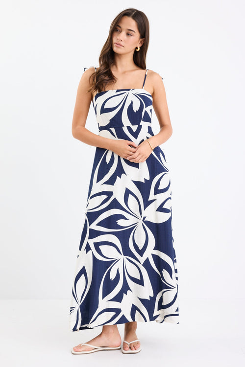 Woman wearing a navy and white printed maxi dress with tie straps, shirred back, and a flowing full-length silhouette.