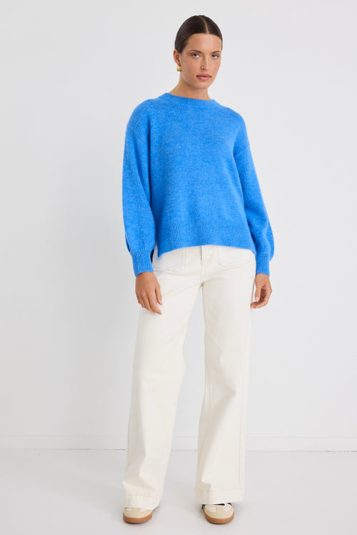 Model wears a azure blue long sleeve knit jumper with white jeans