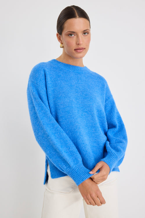 Model wears a azure blue long sleeve knit jumper with white jeans