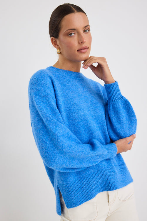 Model wears a azure blue long sleeve knit jumper with white jeans