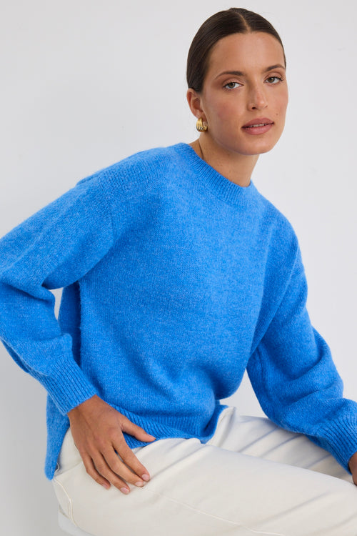 Model wears a azure blue long sleeve knit jumper with white jeans