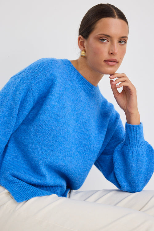 Model wears a azure blue long sleeve knit jumper with white jeans