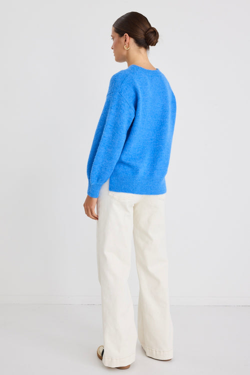 Model wears a azure blue long sleeve knit jumper with white jeans